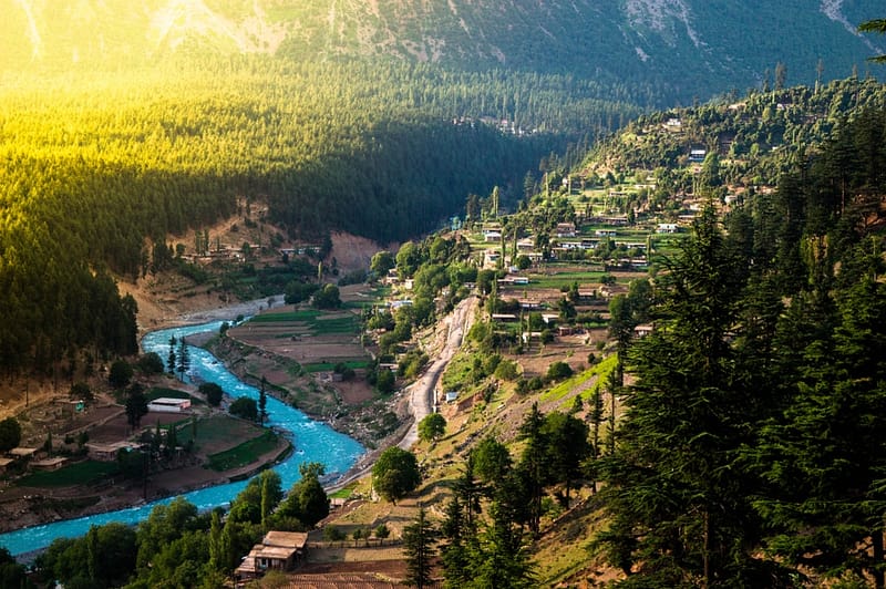 Dhesan Meadows, an enchanting village nestled amidst mountains with a serene river flowing in the background.