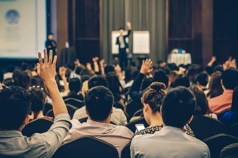 A group of Canadian RV enthusiasts at a conference with their hands raised.