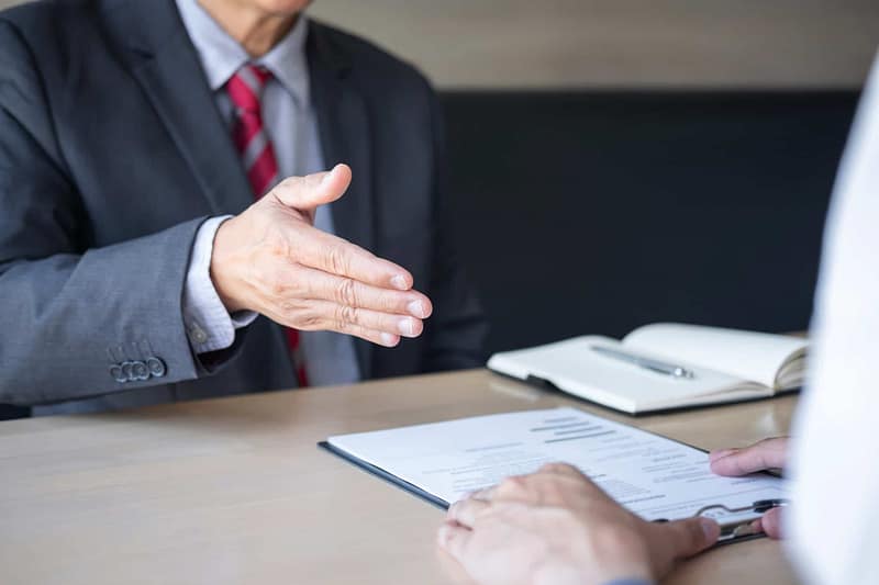A businessman shaking hands with another person at a desk, discussing a proposal.