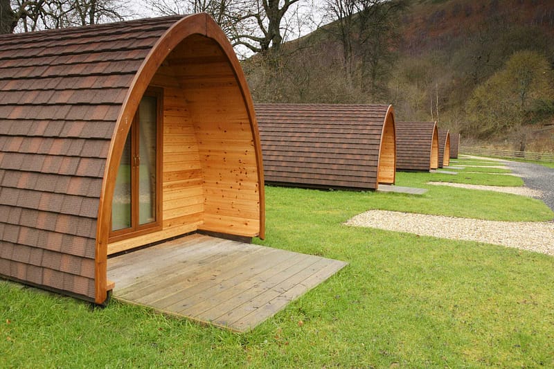An eco-friendly glamping pod expansion proposal in a UK farm, featuring a row of wooden cabins in a grassy area.