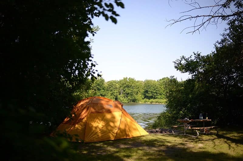 A tent is set up near a body of water at St. Lawrence Parks Campground Reservation.