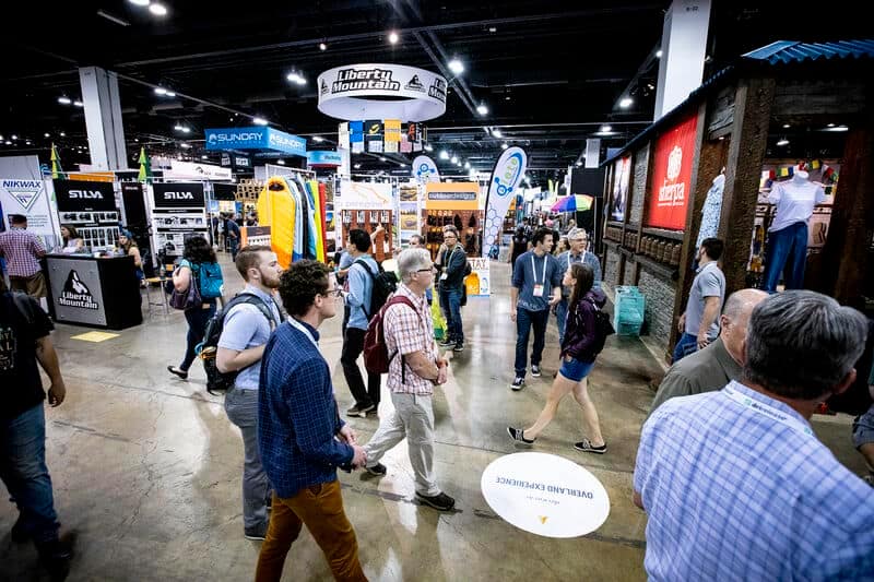 A crowd of people walking through an Industry Association convention hall.