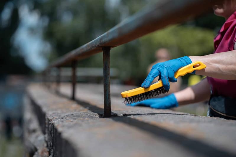 A woman cleaning a railing with a brush as part of the renovation at Mississippi State Parks.
