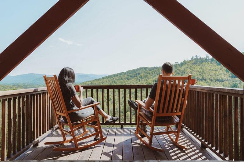 Two people sitting in rocking chairs on a deck overlooking a unique mountain view at Jellystone Parks.