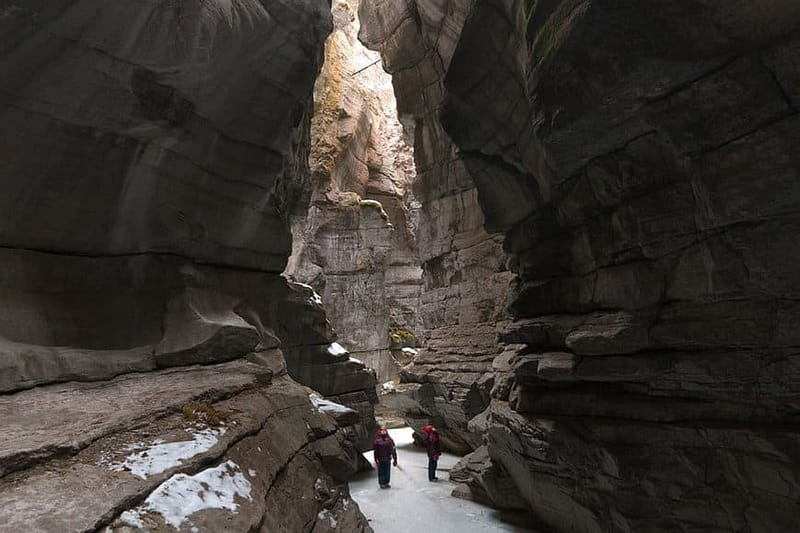 Two people walking through a narrow canyon in Jasper National Park.
