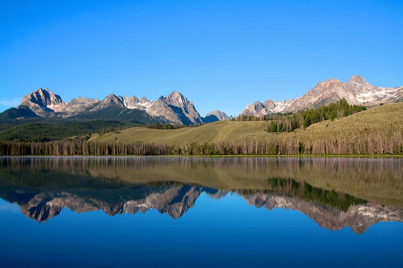 The grand teton mountain range is reflected in a lake surrounded by campgrounds.