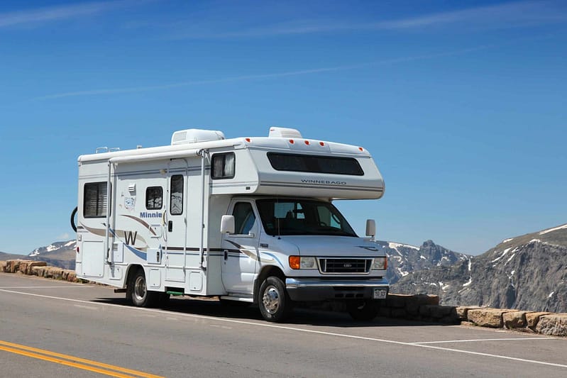 A white Winnebago Industries rv parked on the side of a mountain road.