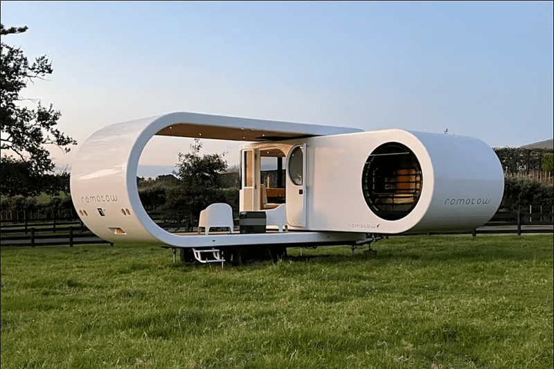 An affordable small white house in the middle of a field with a swinging RV nearby.