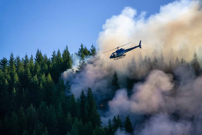 A helicopter flies over a forest fire, engulfed in thick smoke caused by Canadian wildfires.