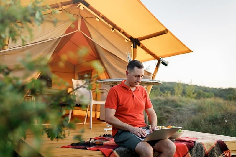 A man working on his laptop in front of a tent at a campsite in New England, gaining insights.