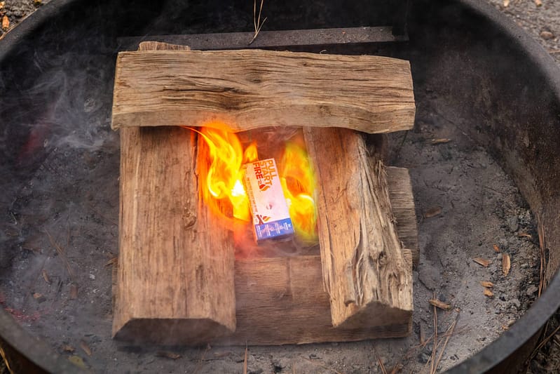 Using the pull start fire method, a piece of wood is safely burning in a fire pit.