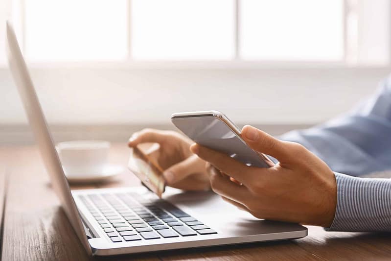 Person using a smartphone to make GRCA camping reservations while working on a laptop at a desk.