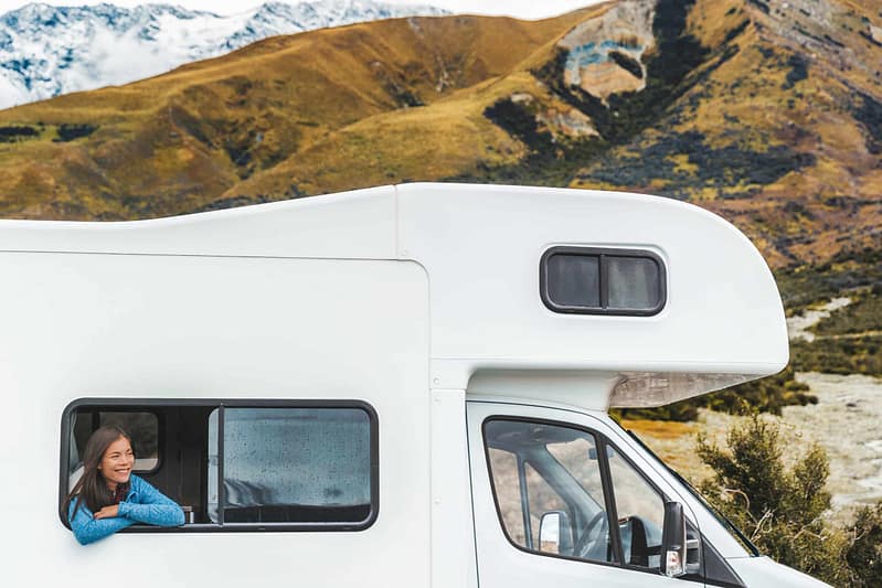 Woman looking out from the window of her RV with scenic mountainous landscape in the background, reflecting the latest trends in RV industry.