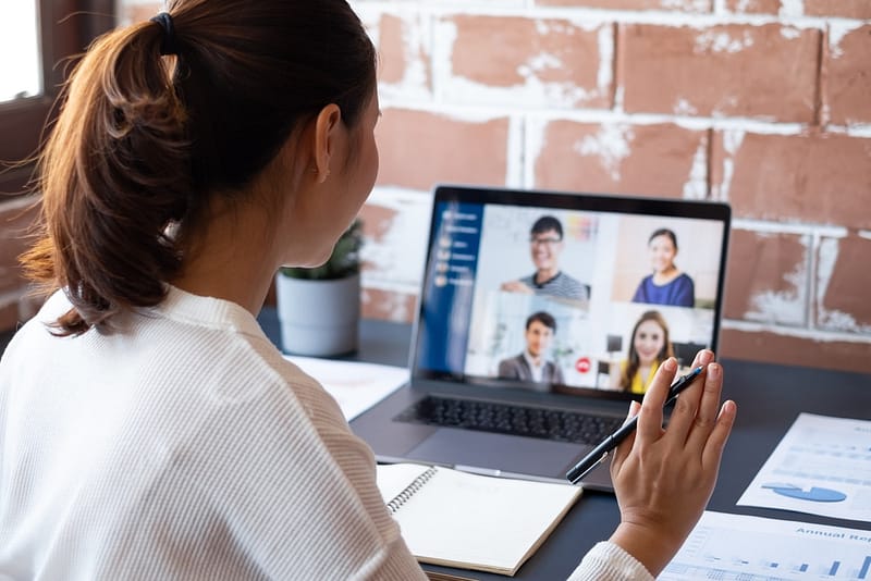 A woman is sitting at a desk with a laptop and a phone in front of her, working virtually.
