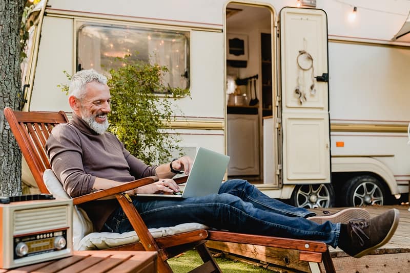 A man sitting in a lawn chair with a laptop in front of an rv.