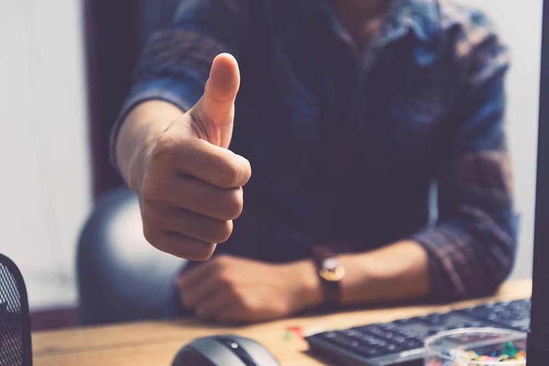A man giving a thumbs up in front of a computer, recommended for approval.