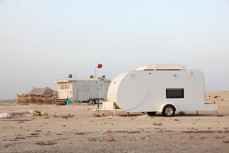 A white camper parked on the sandy beach in Qatar, providing a unique winter camping experience close to nature.