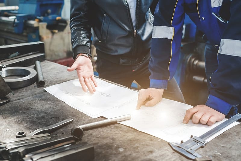 Two men working on a piece of paper in a workshop.