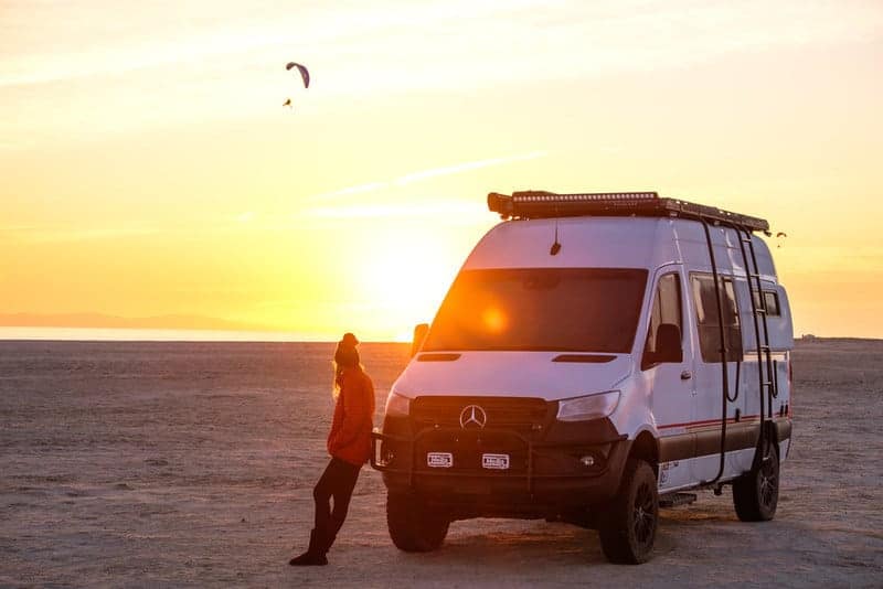 The GoCamp storyteller is standing next to a camper van on the beach.