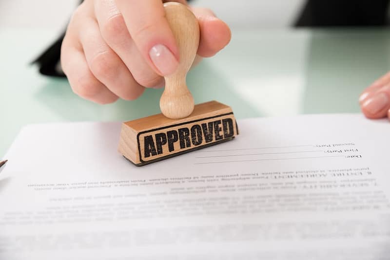 A person is stamping a document with the word approved.