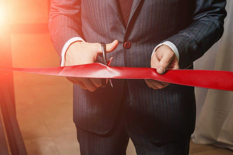 A man in a suit cutting a red ribbon.