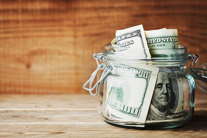 A proposed glass jar filled with money on a wooden table in New York at Sacandaga RV Park.