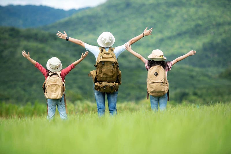 Three children participating in the Virginia Residents Tourism Program, standing in a field with mountains in the background.
