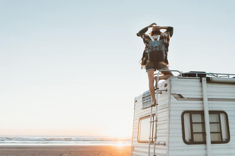 A woman standing on top of a Delmarva RV Sales camper on the beach.