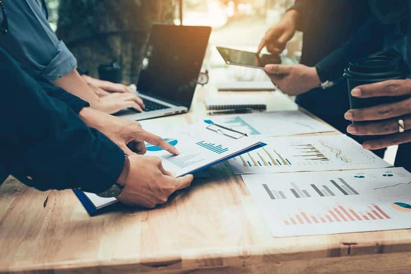 A group of Sales Leadership business people looking at Octane graphs on a table, which strengthens their strategies and decision-making.