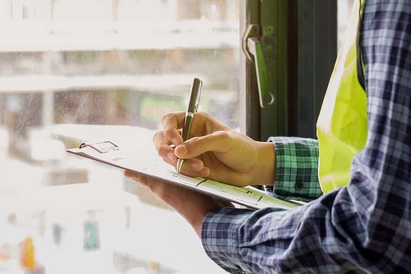 A construction worker from the Industry Association writing on a clipboard in front of a window.