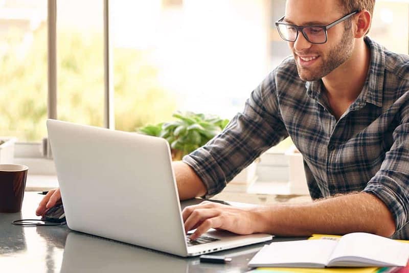 A man sitting at a desk using a laptop with Campspot's online cancellations feature.
