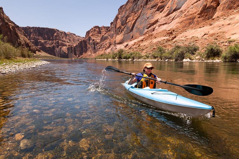 A woman is kayaking down a river in an outdoor recreation industry setting.