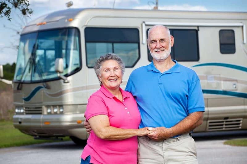 An Australian couple standing in front of an RV at a Caravan Park, enjoying a Tourism Experience.