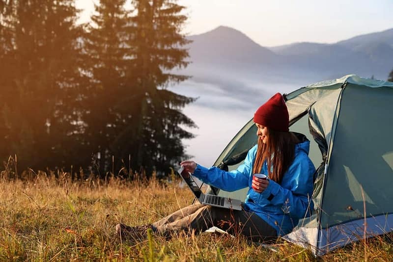 Today's camper is sitting in front of a tent with a laptop, researching tech upgrades.
