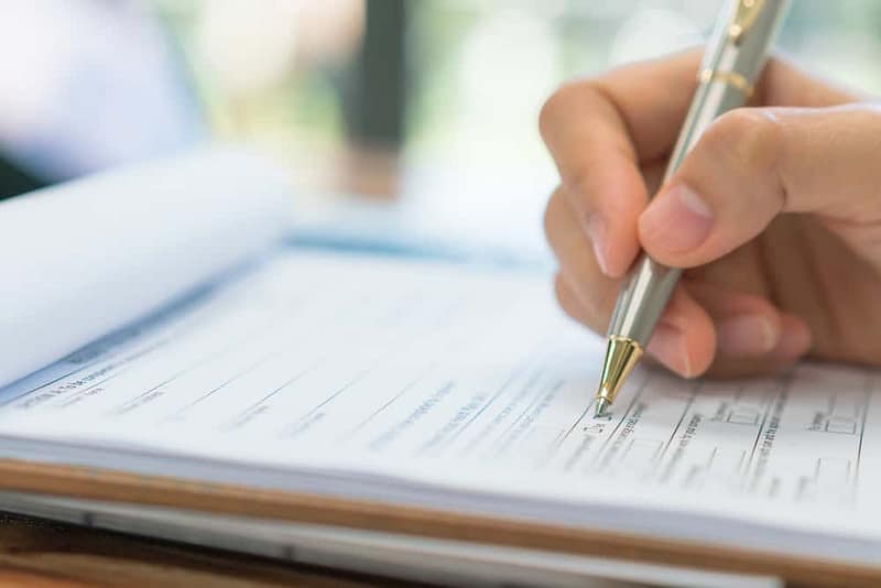 A person writing applications on a paper with a pen.