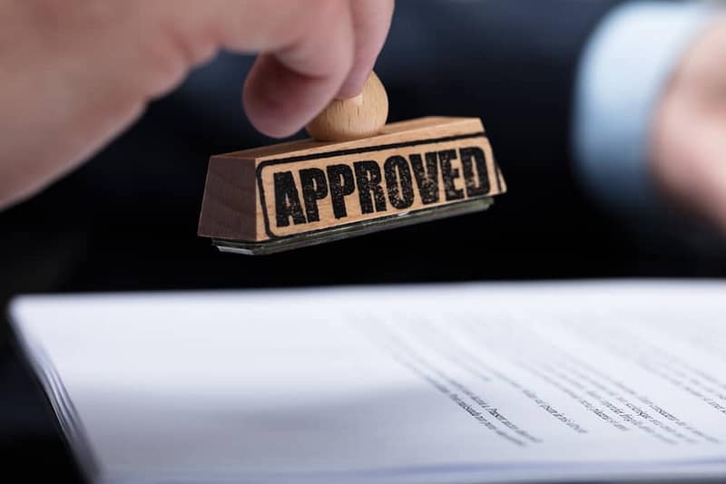 A man is holding a rubber stamp with the word compliance approval on it.