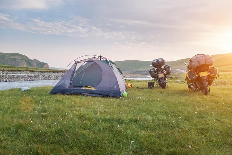 Two motorcycles and a tent set up in a grassy field, showcasing the emerging camping tourism development in China.