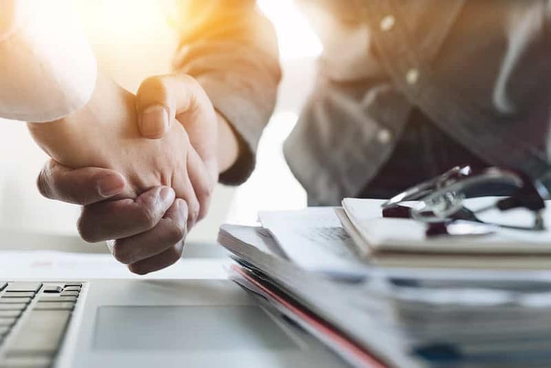 Two business people shaking hands in front of a laptop while Cedarline Outdoor acquires Jonestown / Hershey KOA Campground.