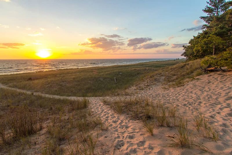 The sun is setting over the sand dunes at Muskegon State Park beach, which is known for its stunning views and relaxing atmosphere. The park has recently received funding to improve its amenities