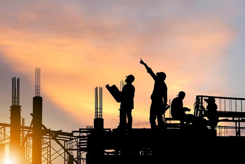 Silhouettes of construction workers on a development site at sunset, during the 2nd phase.