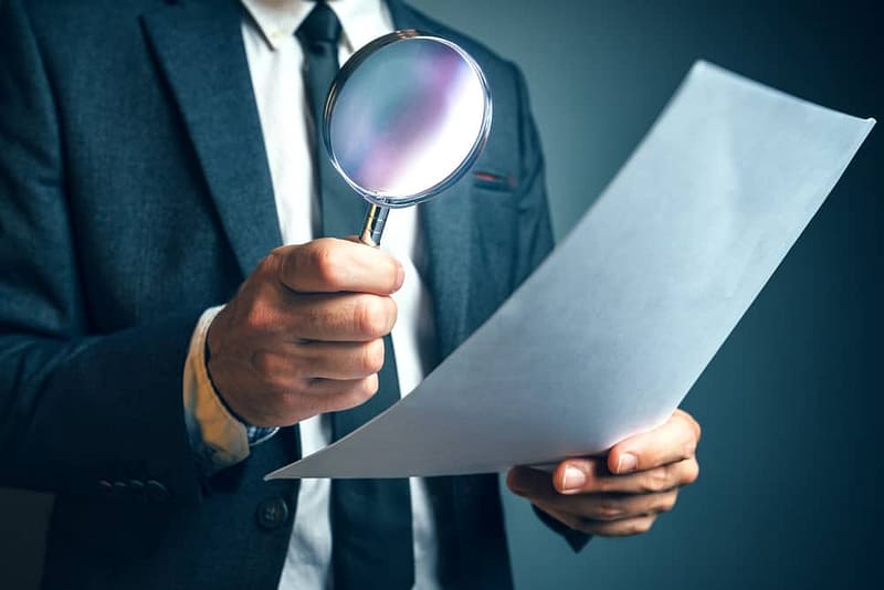 A man in a suit holding a magnifying glass inspects an RV.