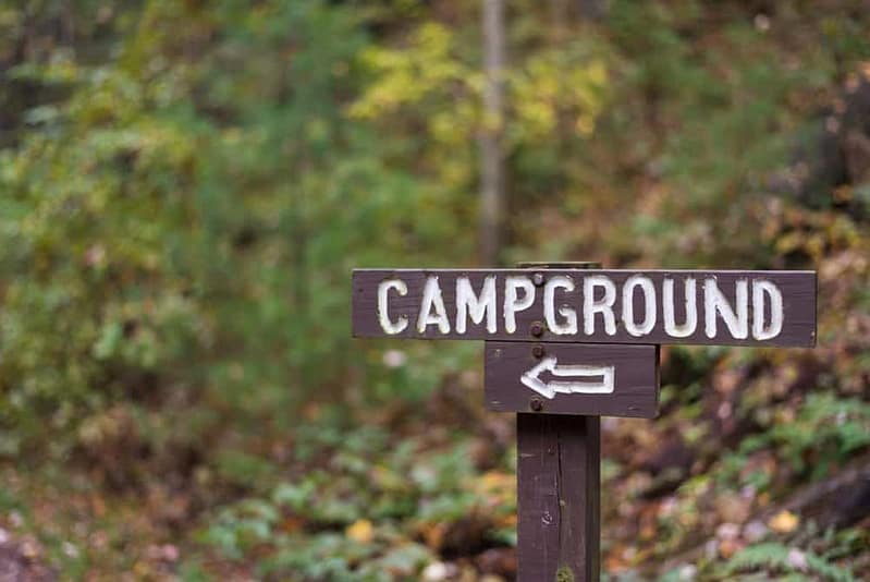 A wooden sign pointing to a campground in the woods, attracting campers and campground owners interested in growth strategies for their campspot.