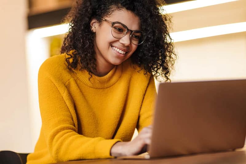 A young woman smiling while using a laptop to receive instant answers from an AI chatbot, experiencing unmatched convenience.