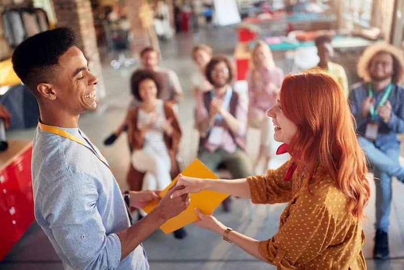 A man and a woman shaking hands in front of a group of people during the RV industry's Fixed Operations Certification Week.