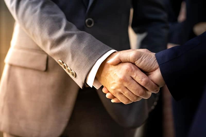 Two business people from Pan Pacific RV Center and Camping World shaking hands in front of each other as they finalize their acquisition agreement.