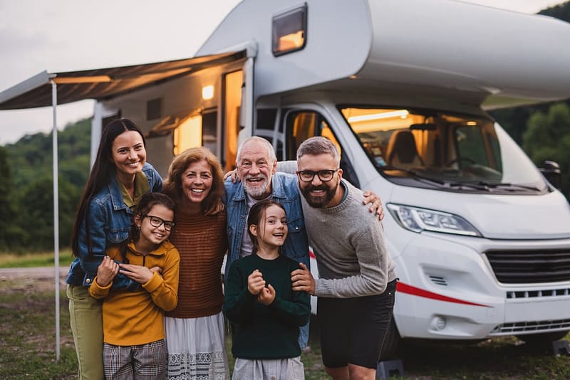 A enthusiastic family posing in front of an RV during a camping trip on Memorial Day.