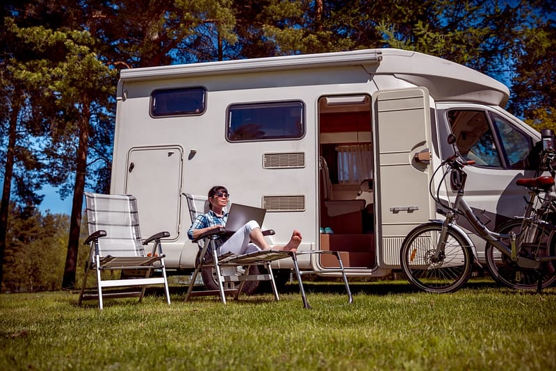 An innovative woman sits in front of an rv with a laptop, immersed in the user experience of the RV industry.