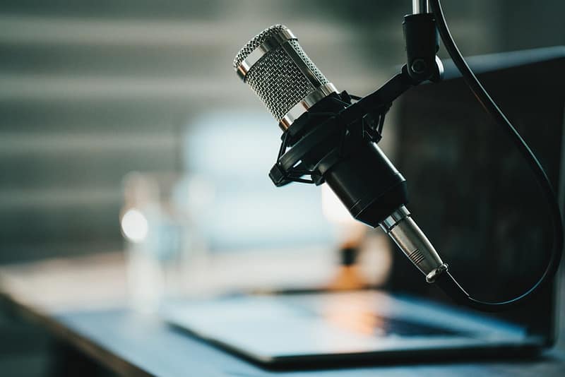 A microphone sits on a desk next to a laptop as Joel Holland, the CEO and founder of Harvest Hosts, shares his success story.