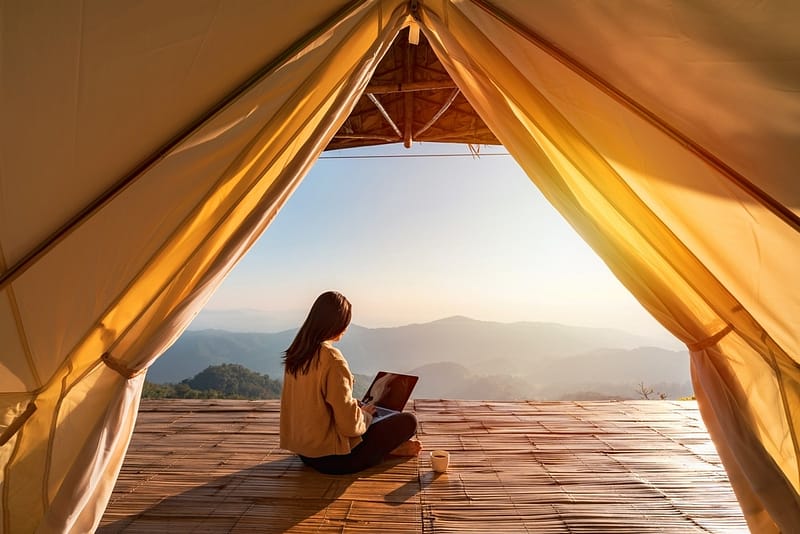 A woman is sitting in a tent with a laptop, enjoying the outdoors while browsing Property Offerings.