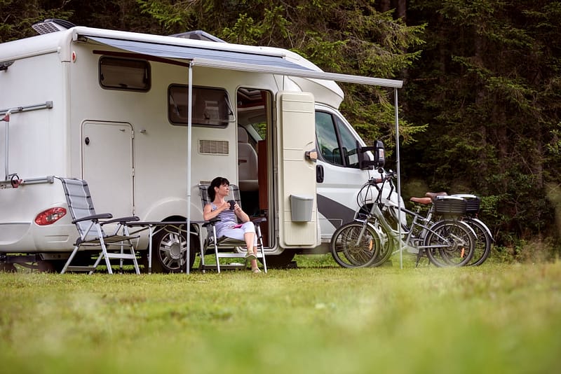 A woman sits in front of an rv with a bicycle in front of it.